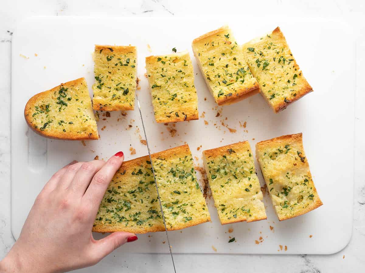 Homemade Garlic Bread is twice as nice for half the price of it's frozen store bought counterpart! An inexpensive and freezer-friendly side dish! BudgetBytes.com Garlic bread loaf being cut into pieces on a cutting board.