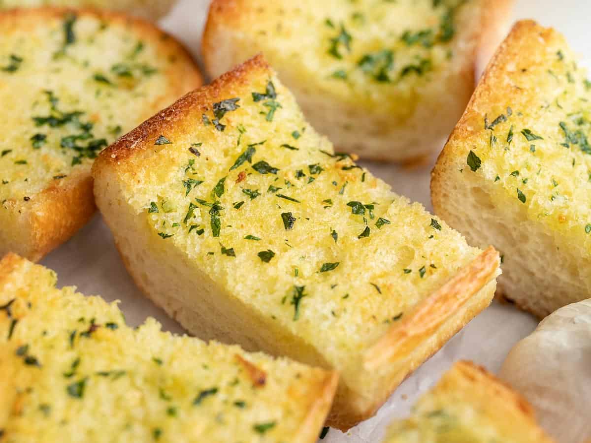 Homemade Garlic Bread is twice as nice for half the price of it's frozen store bought counterpart! An inexpensive and freezer-friendly side dish! BudgetBytes.com Close up side view of slices of garlic bread.