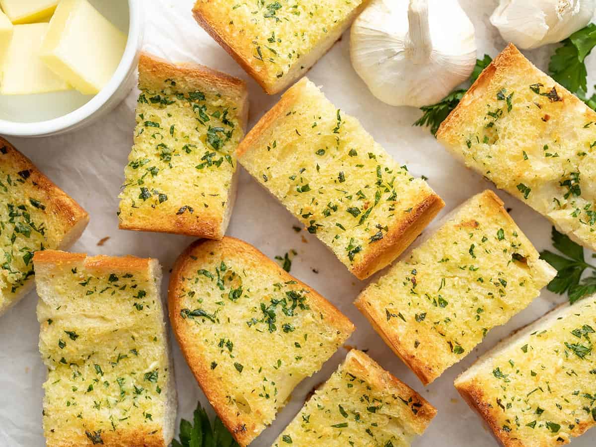 Homemade Garlic Bread is twice as nice for half the price of it's frozen store bought counterpart! An inexpensive and freezer-friendly side dish! BudgetBytes.com Slices of homemade garlic bread spread out on a surface.