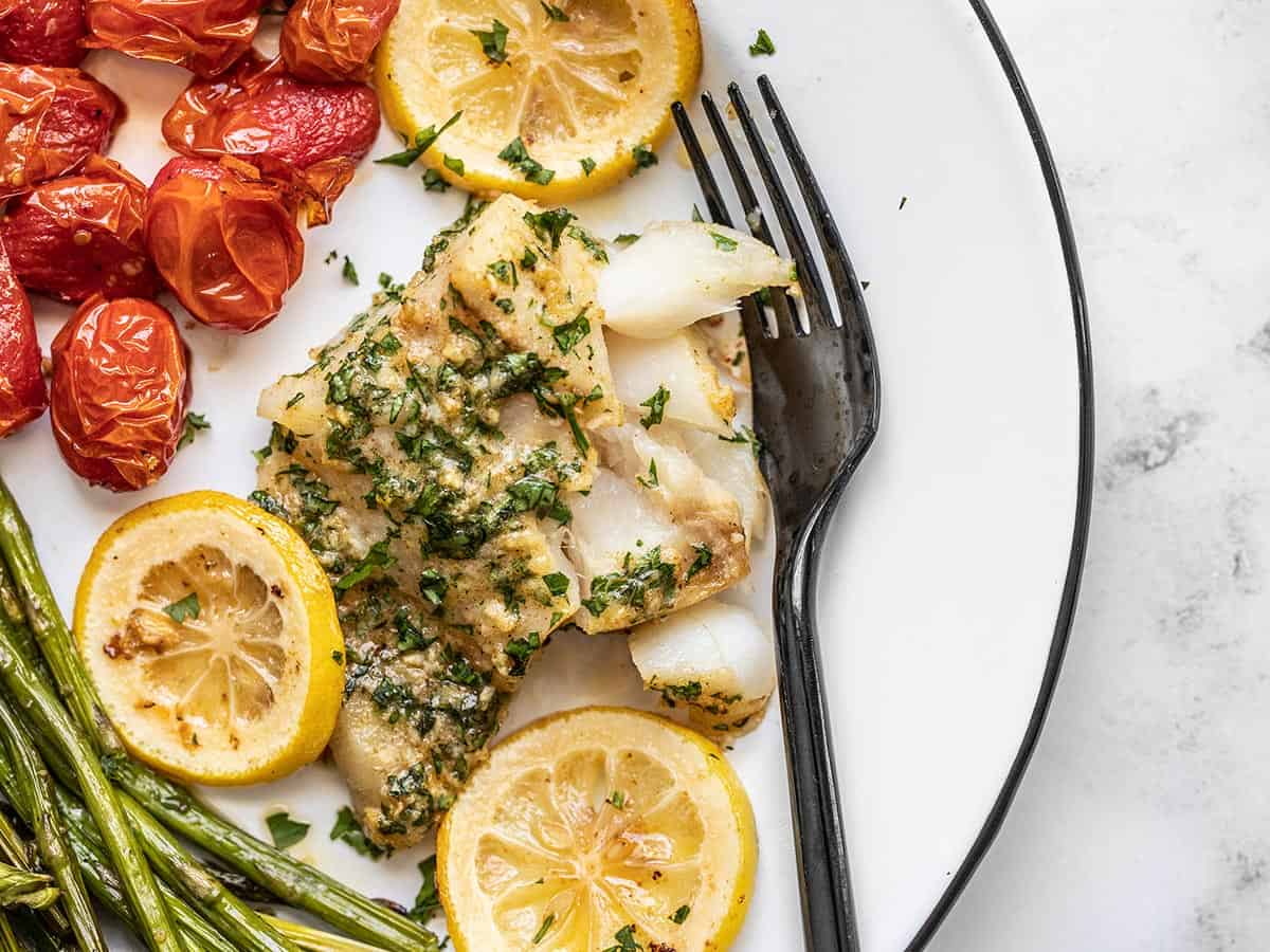 Garlic butter baked cod on a plate with roasted tomatoes and asparagus.
