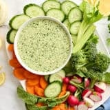 Overhead view of a bowl of green goddess dressing with a plate of fresh cut vegetables.