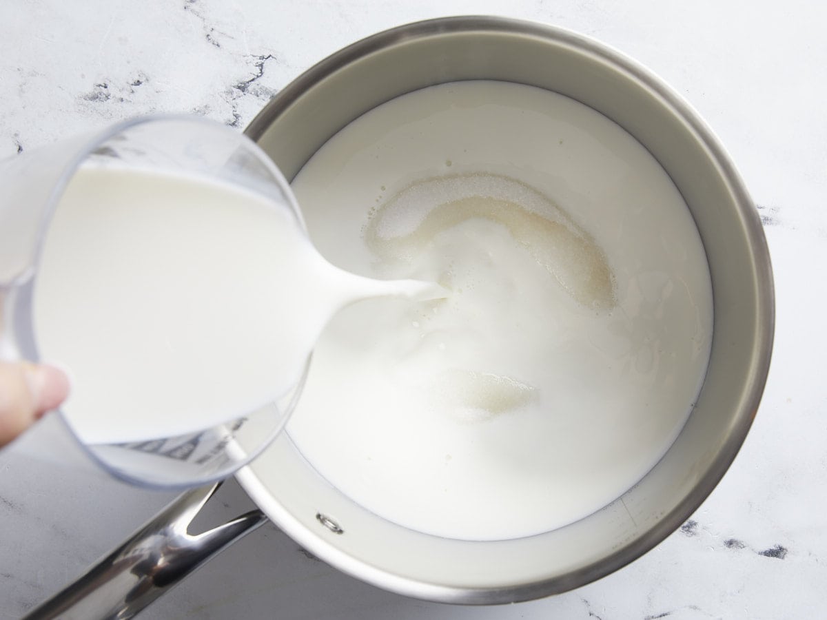 Milk pouring into a sauce pan with sugar.