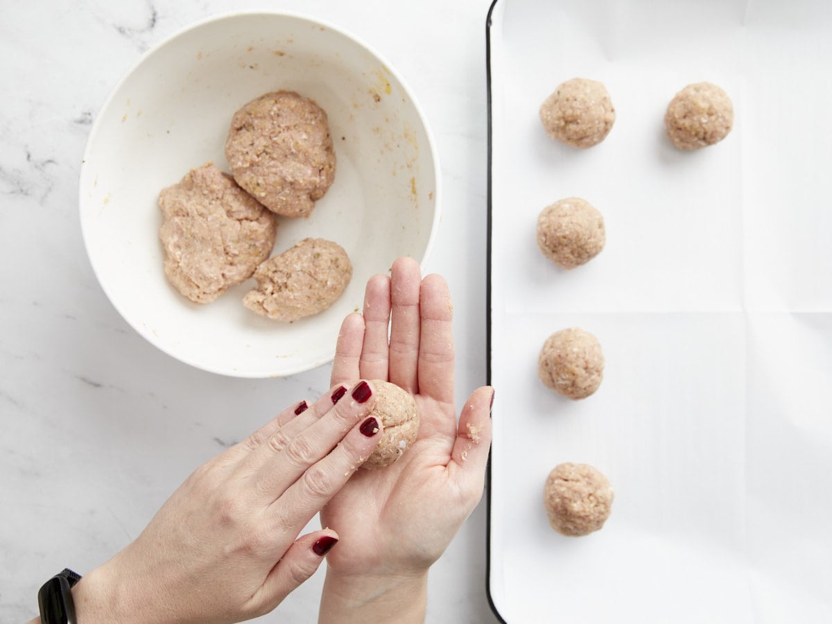 Meatballs being shaped and placed on a sheet pan.