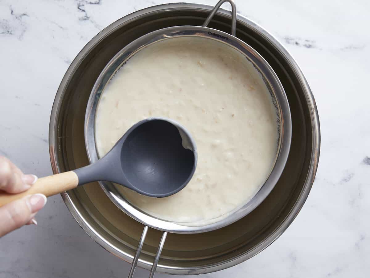 Coconut and milk mixture being strained through a sieve.