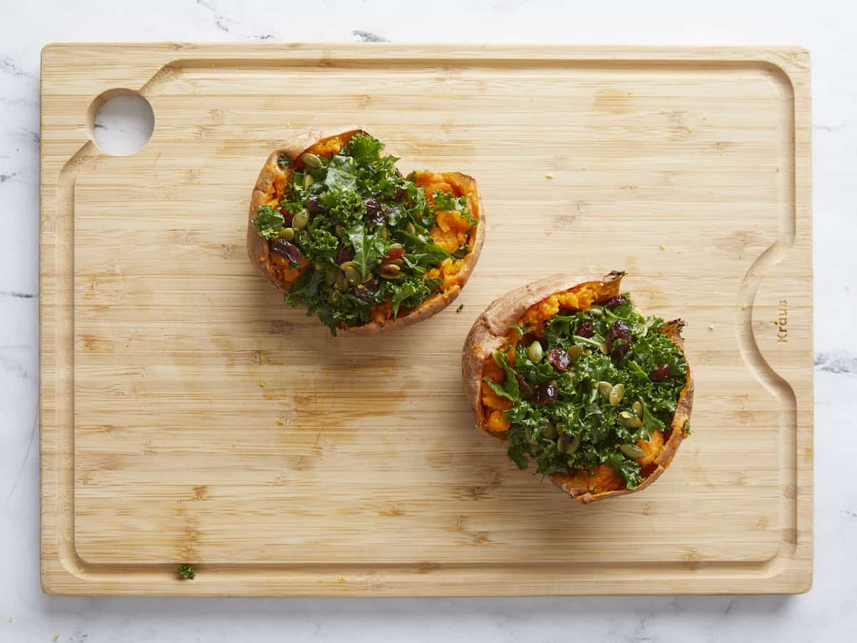 Sweet potatoes stuffed with kale on a wooden cutting board.