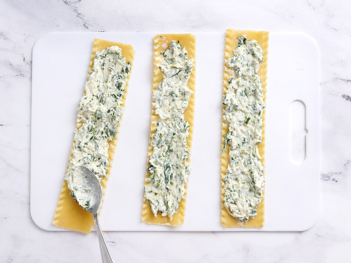 A spoon adding spinach and ricotta filling to a lasagna noodle.