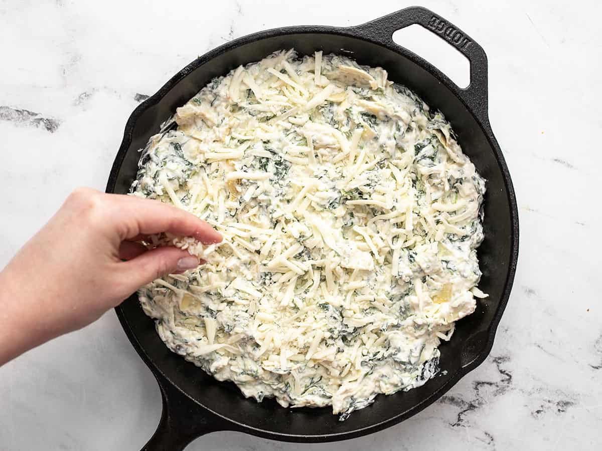 Spinach artichoke dip added to a skillet, mozzarella being sprinkled over top.