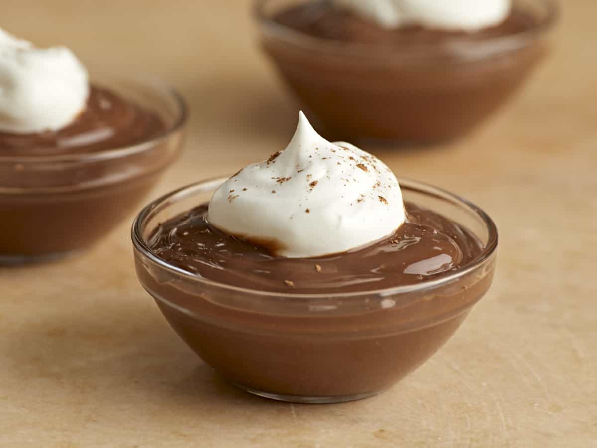 Close up side view of small dishes of chocolate pudding with whipped cream.