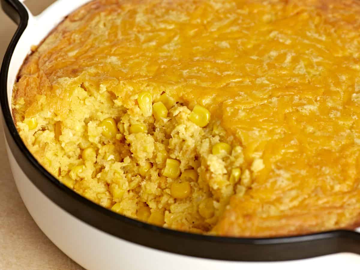 Side view of corn pudding in the casserole dish with some scooped out.