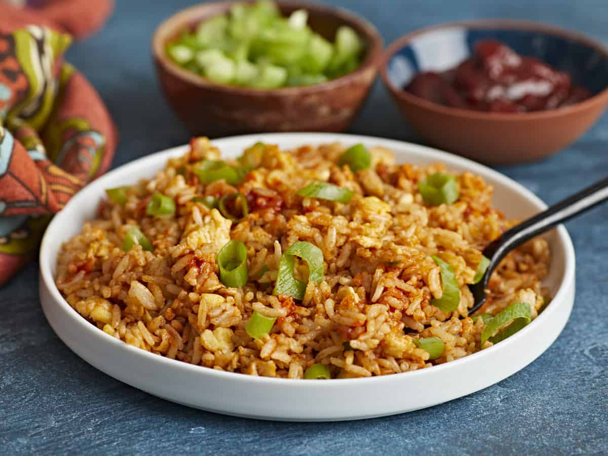 Side view of a plate full of scrambled eggs with rice and a fork in the side.