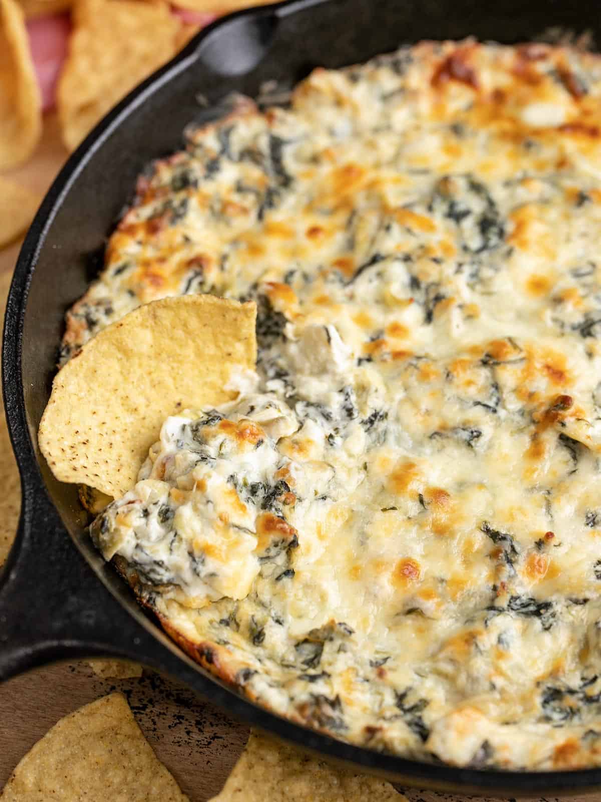 Double Spinach Artichoke Dip is PACKED with spinach, three types of cheese, and just enough spice to tingle your taste buds. It’s the classic dip, elevated. BudgetBytes.com Close up side view of a skillet full of spinach artichoke dip with a tortilla chip.
