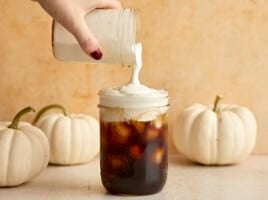 Sweet Cream Cold Foam being poured over a jar full of iced coffee.