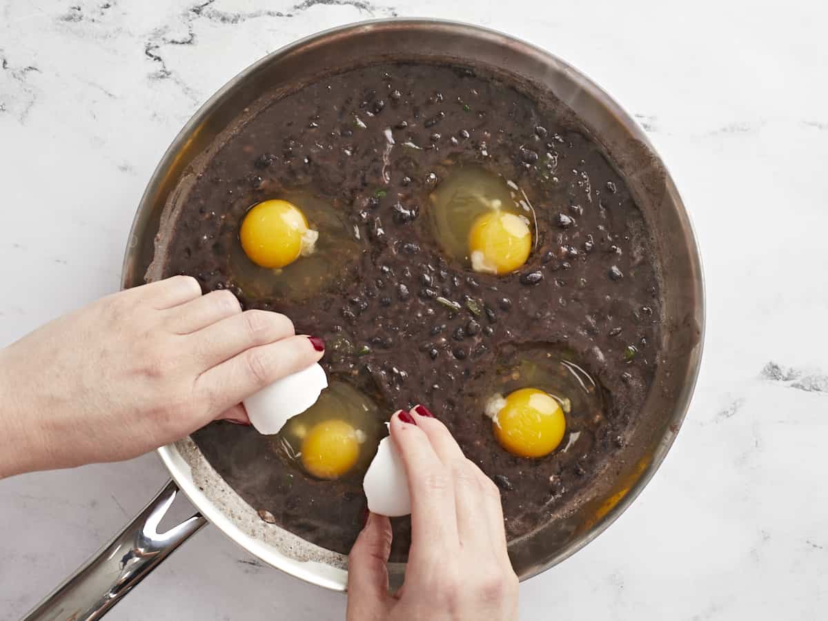 Eggs being cracked into the skillet of black beans.
