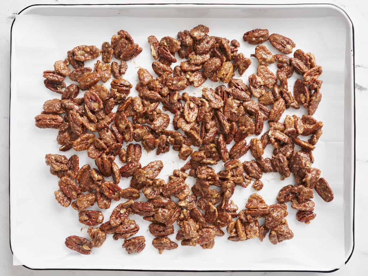 Candied pecans spread onto a baking sheet, ready to bake.