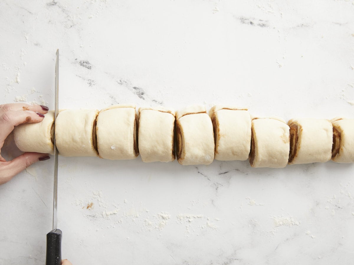 Rolled dough being sliced into rounds.