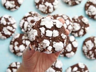 A hand holding a chocolate crinkle cookie close to the camera with others in the background