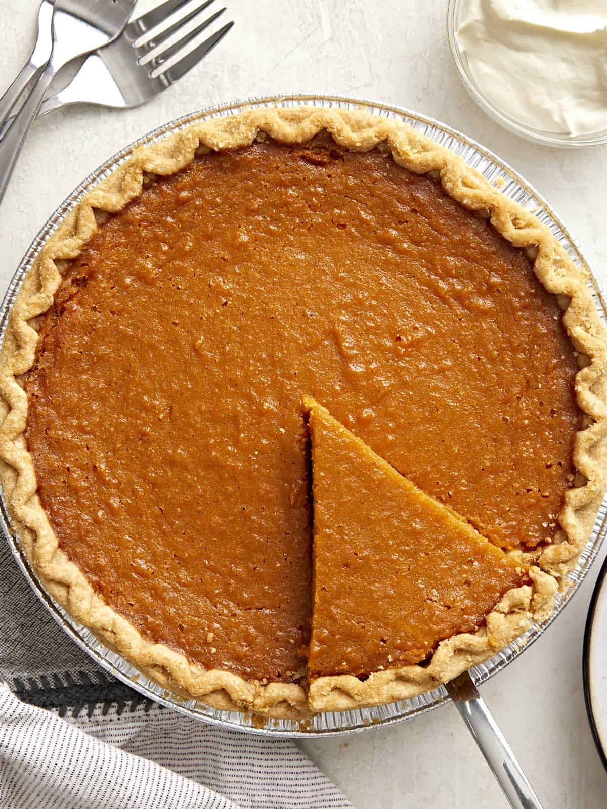 Overhead view of a whole sweet potato pie with one slice cut and being lifted out of the pie pan.