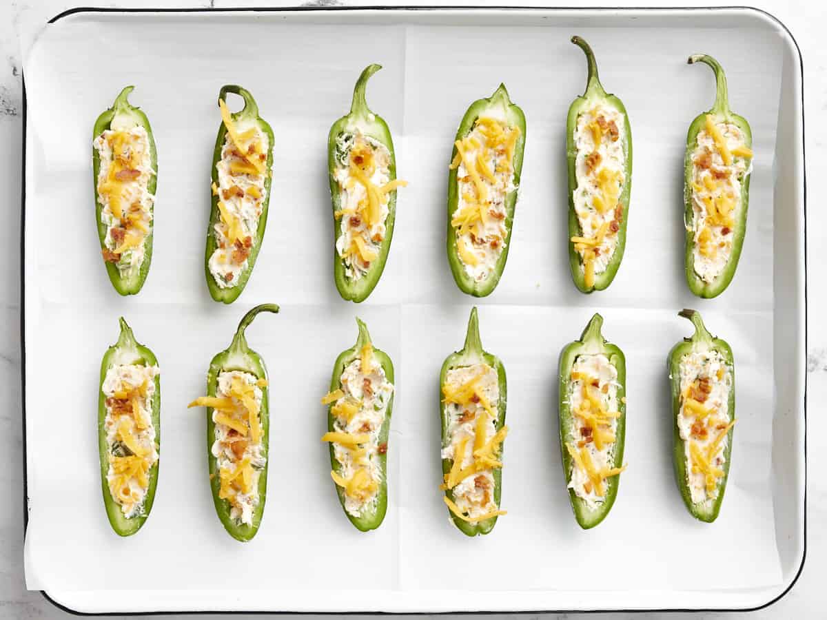 Jalapeño poppers ready to bake on a parchment-lined sheet pan.