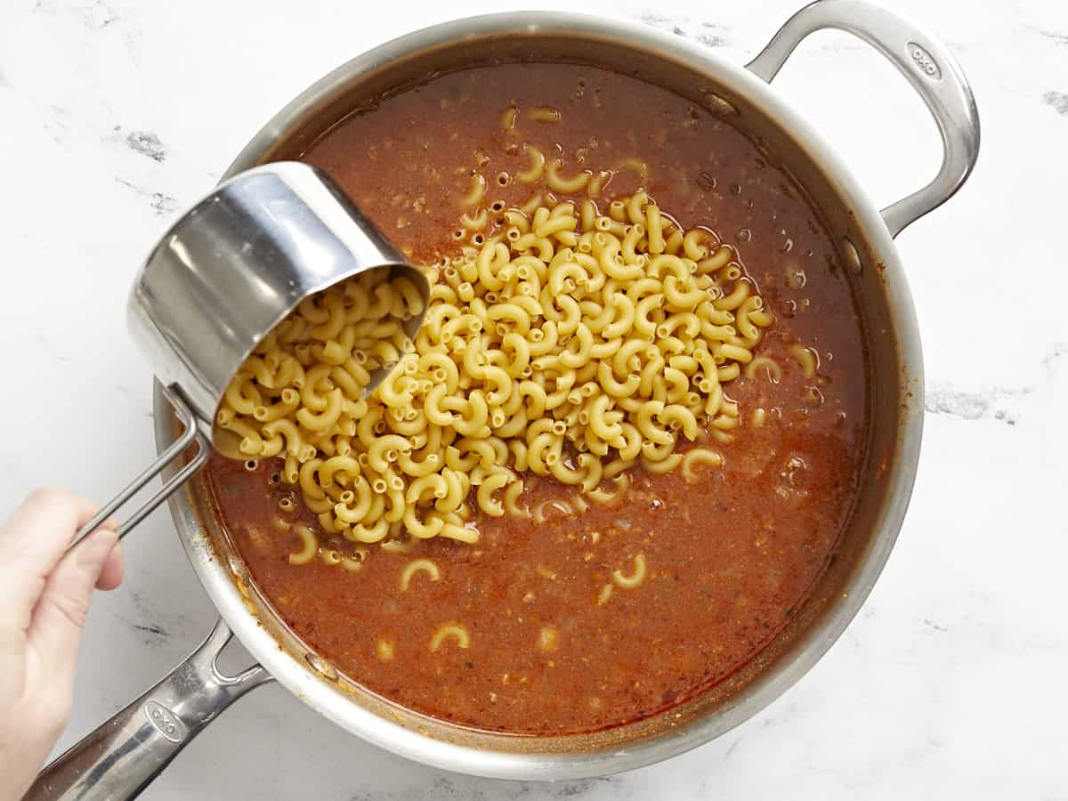 Macaroni being poured into the skillet.