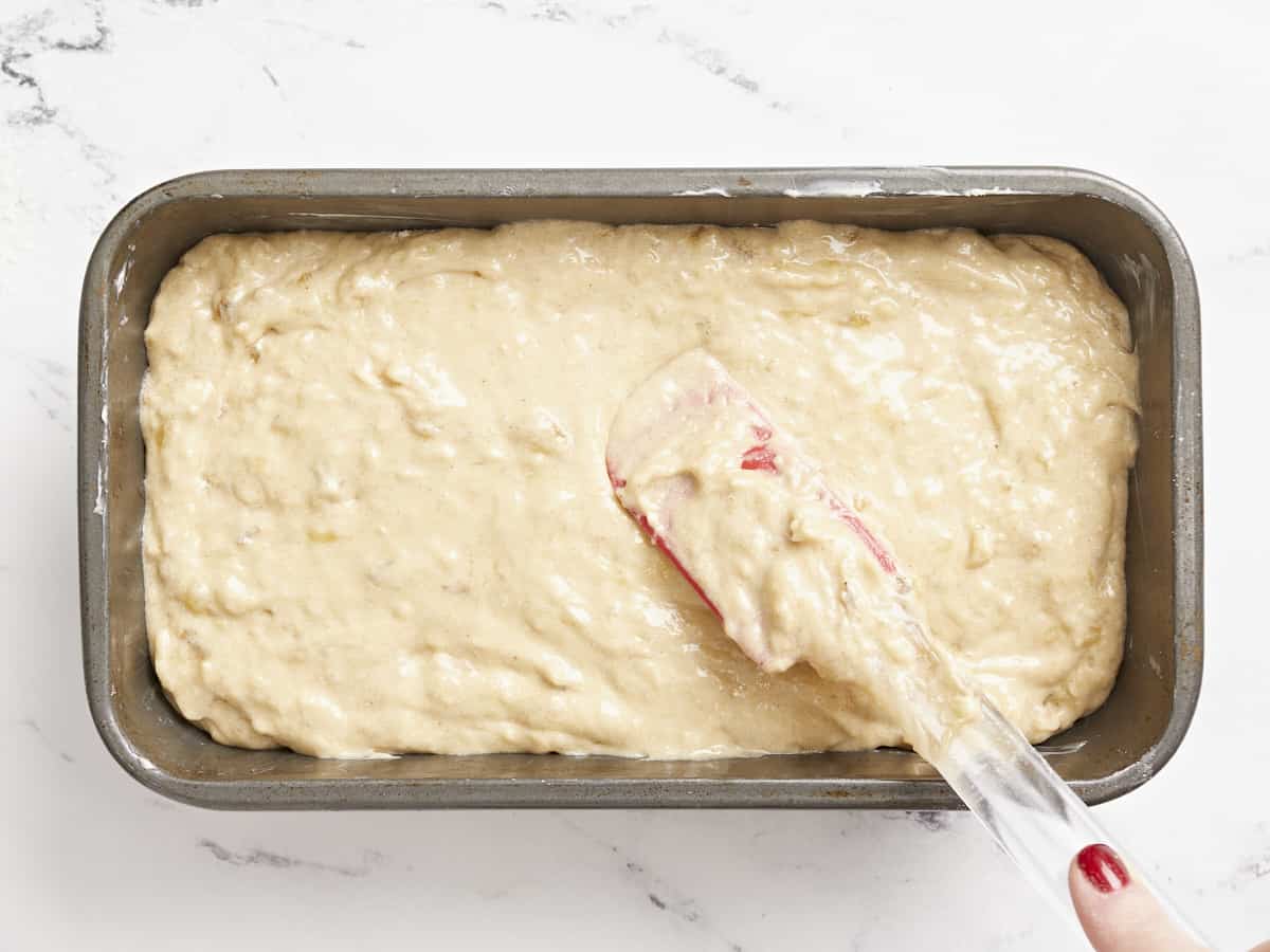 Banana bread batter being smoothed into a bread pan.
