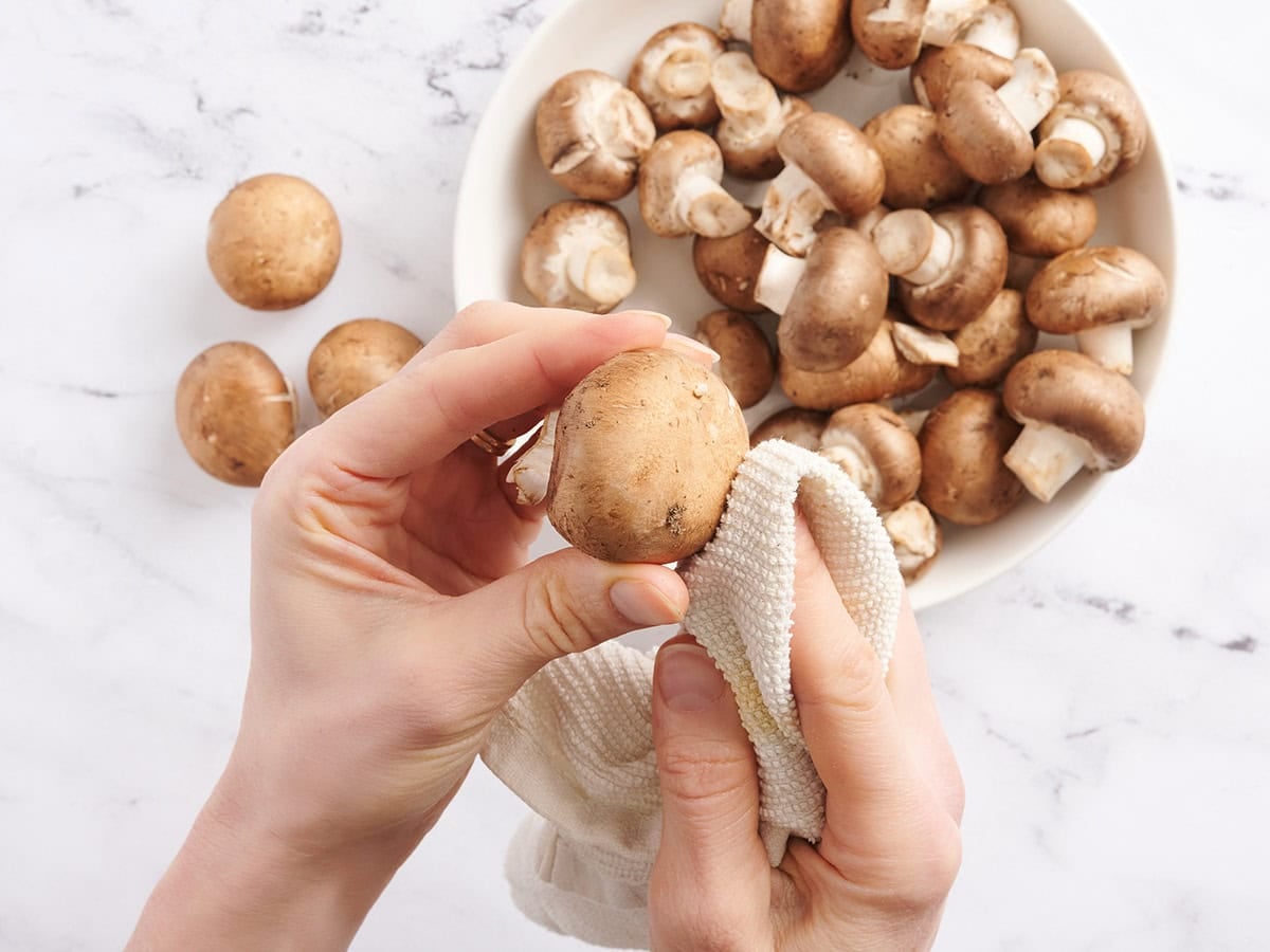 A hand using a towel to clean mushrooms