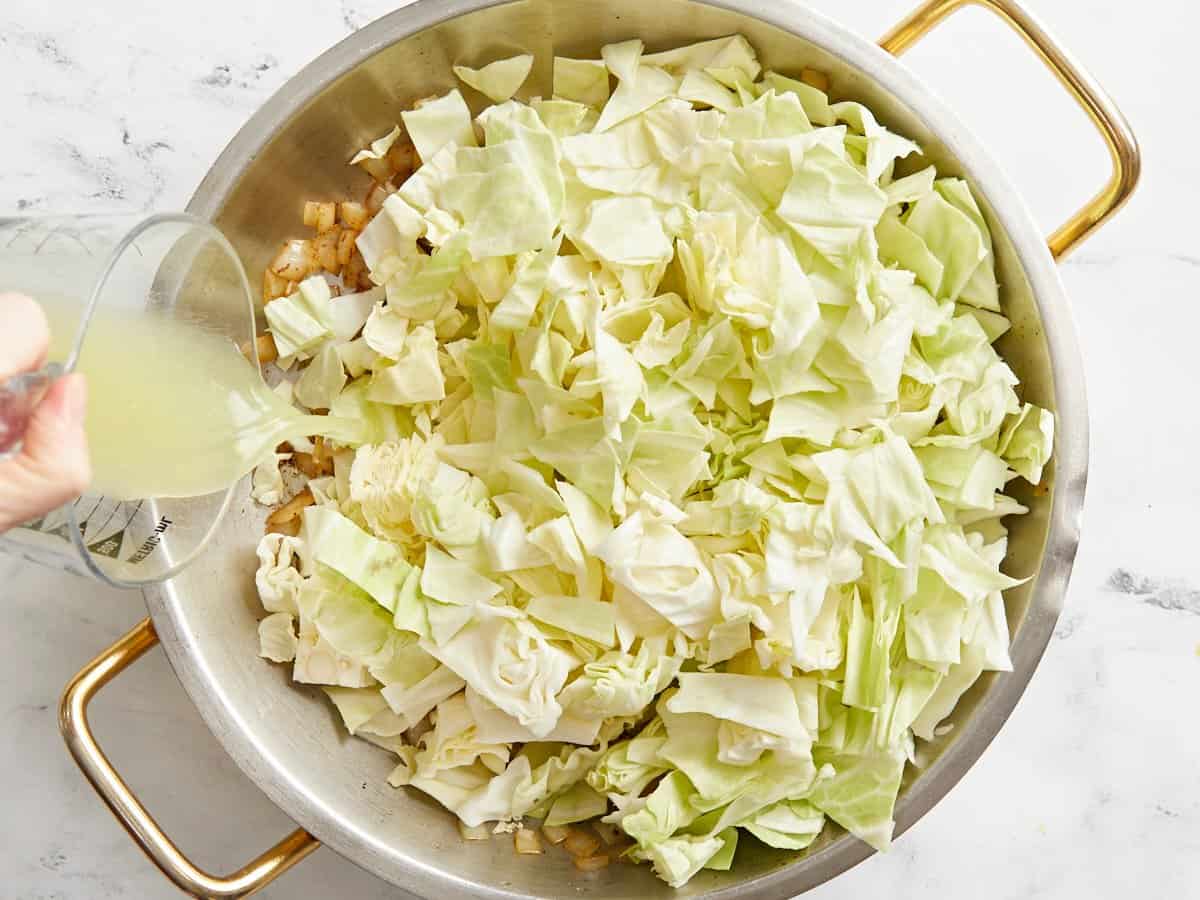 Chopped cabbage added to the skillet, broth being poured into the side.