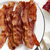 Overhead view of Air Fryer bacon strips on a white serving plate with toast on the side.