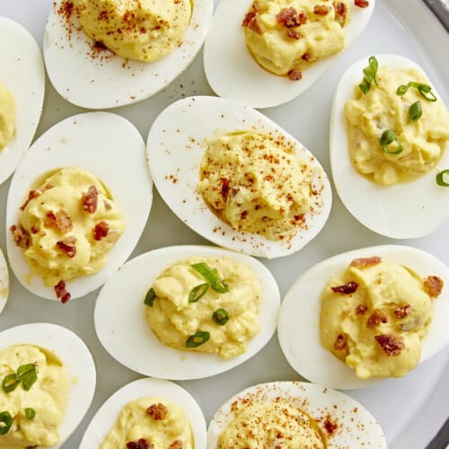 Overhead view of deviled eggs with different toppings on a serving platter.