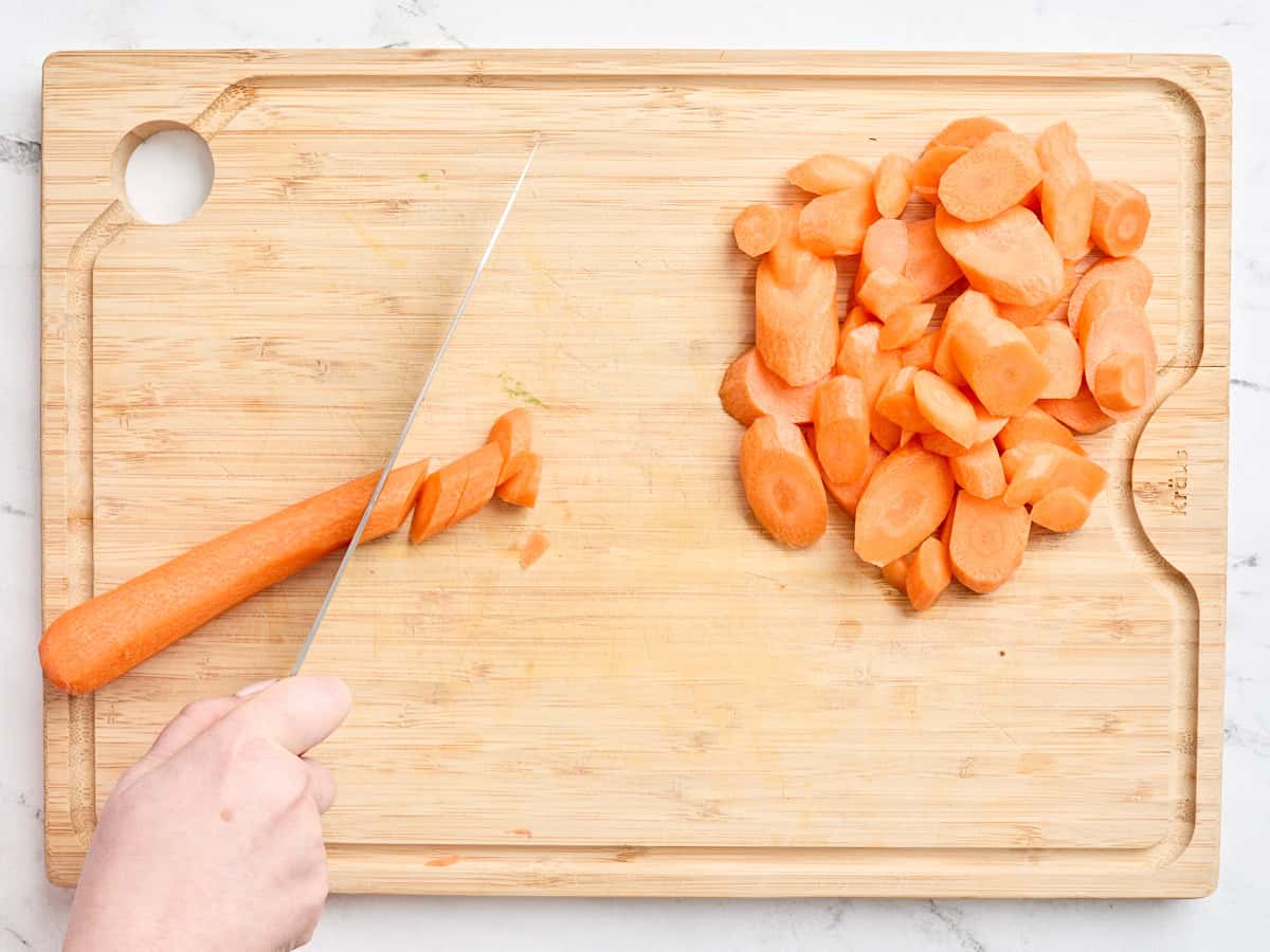 Overhead view of a carrot being chopped on a wooden cutting board.