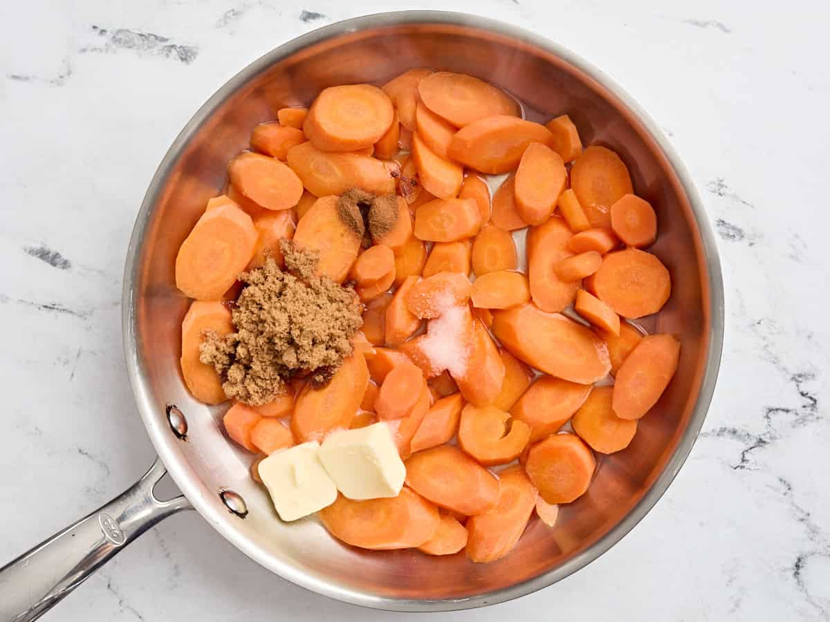 Chopped carrots in a pan with butter, cinnamon, salt, and brown sugar.