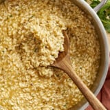 overhead view of a wooden spoon in a pan of parmesan risotto.