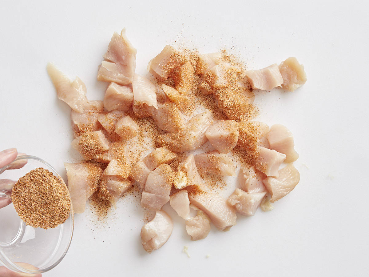 diced chicken breast with seasoning being sprinkled on top.