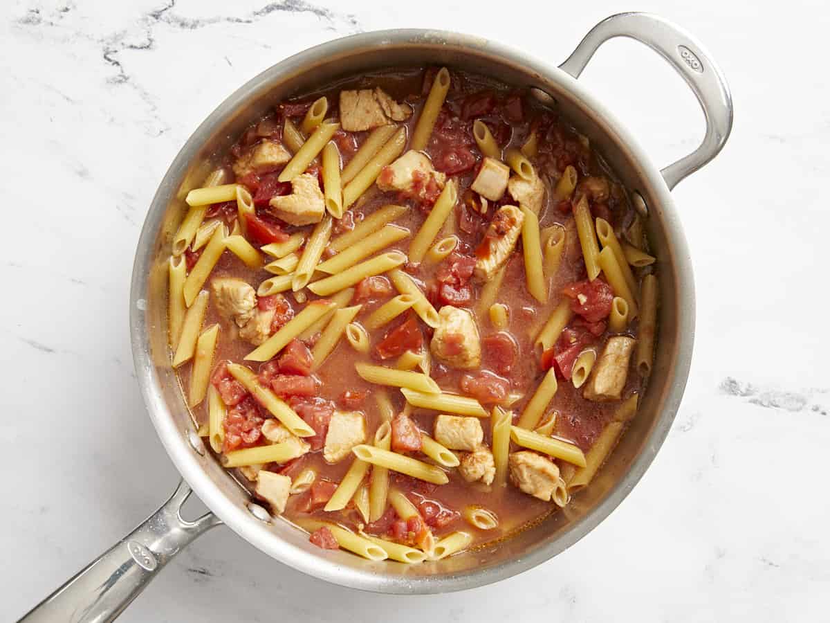 Uncooked pasta in the skillet with the chicken and tomatoes.