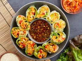 overhead view of kimchi spring rolls on a platter with a bowl of sauce in the middle.