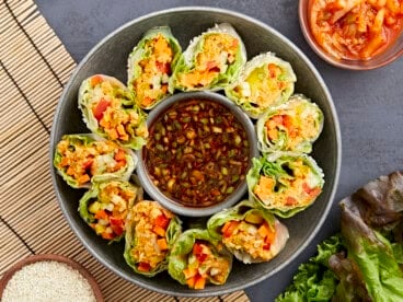 overhead view of kimchi spring rolls on a platter with a bowl of sauce in the middle.