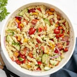 Overhead view of pasta salad in a large white serving bowl with wood serving utensils on the side.