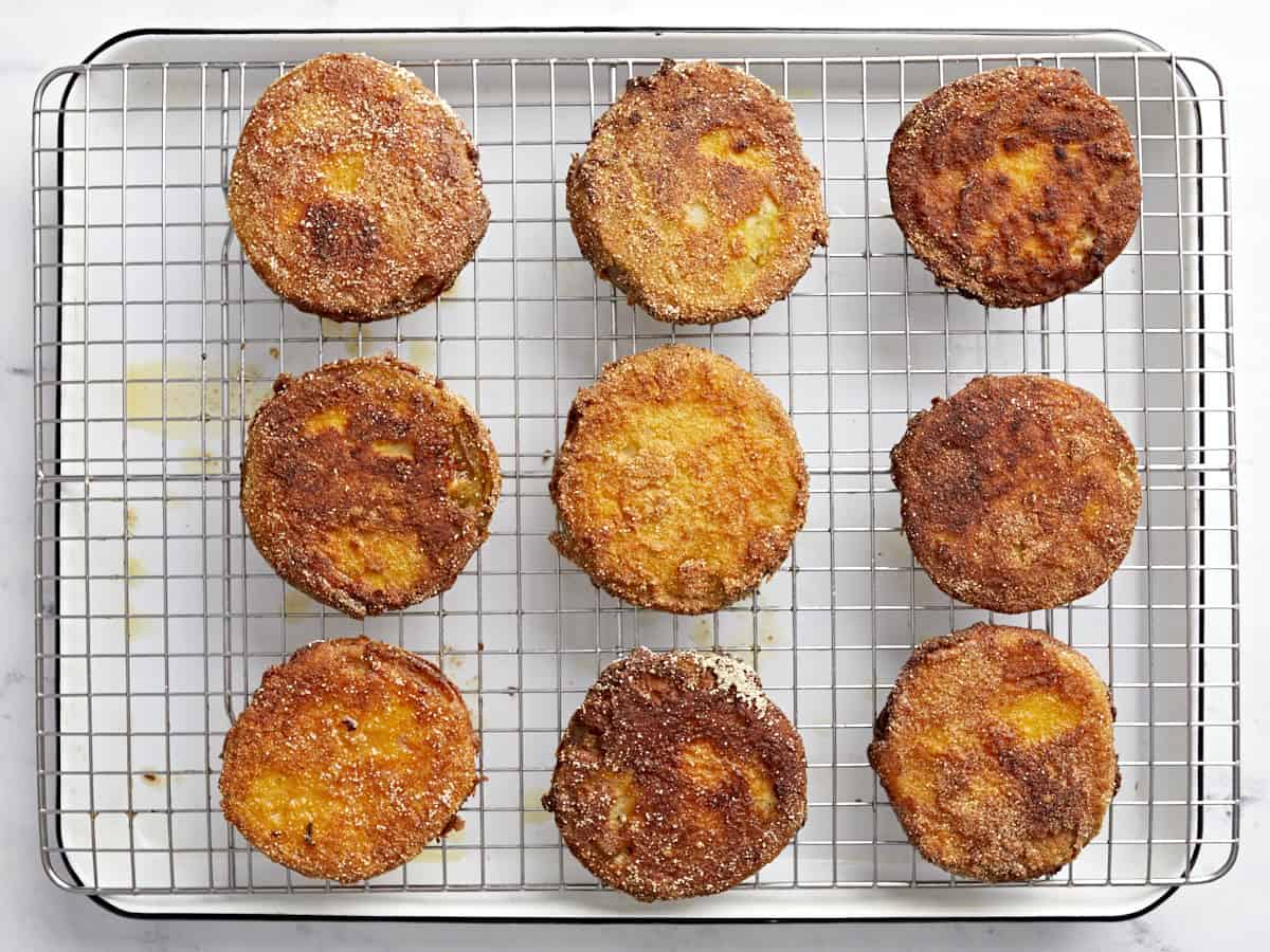fried green tomatoes draining on a wire rack set in a baking sheet.