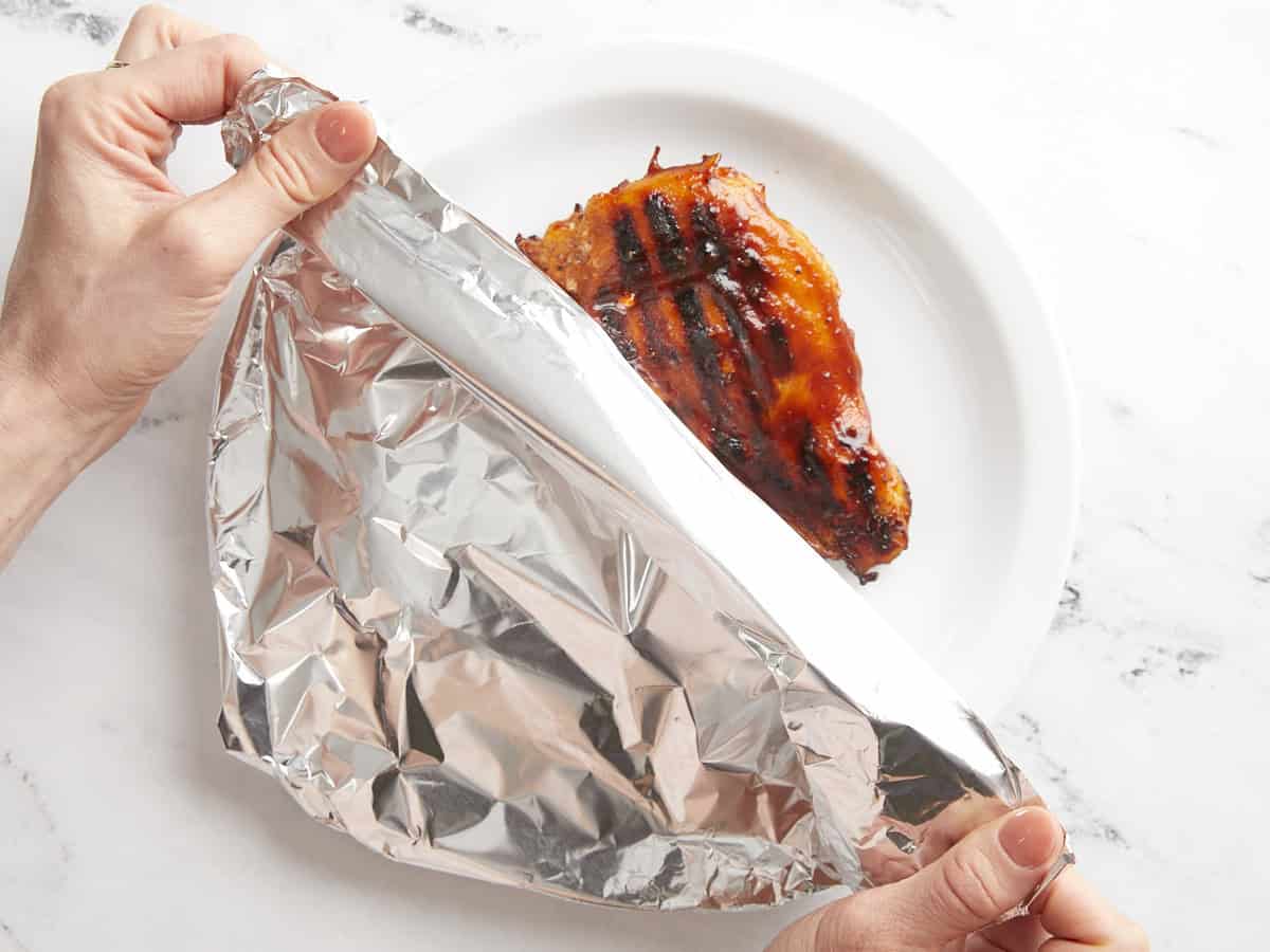Tenting grilled BBQ chicken breasts with foil.