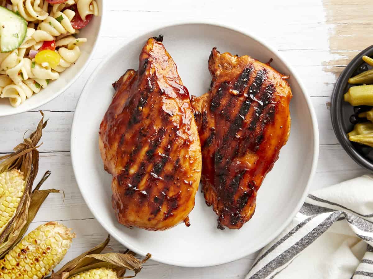 overhead view of 2 grilled bbq chicken breasts on a white plate.