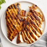 overhead view of 2 sliced grilled chicken breasts on a white plate.