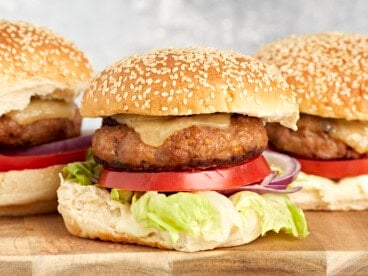side view of turkey burgers topped with cheese, lettuce, and tomato on buns.
