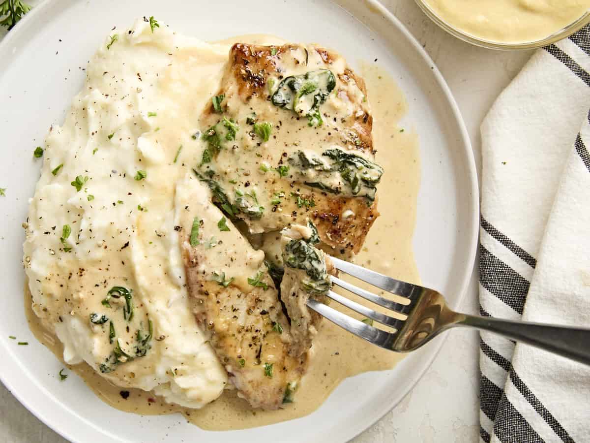 Creamy dijon chicken on a plate with mashed potatoes and a fork lifting some chicken off the plate.