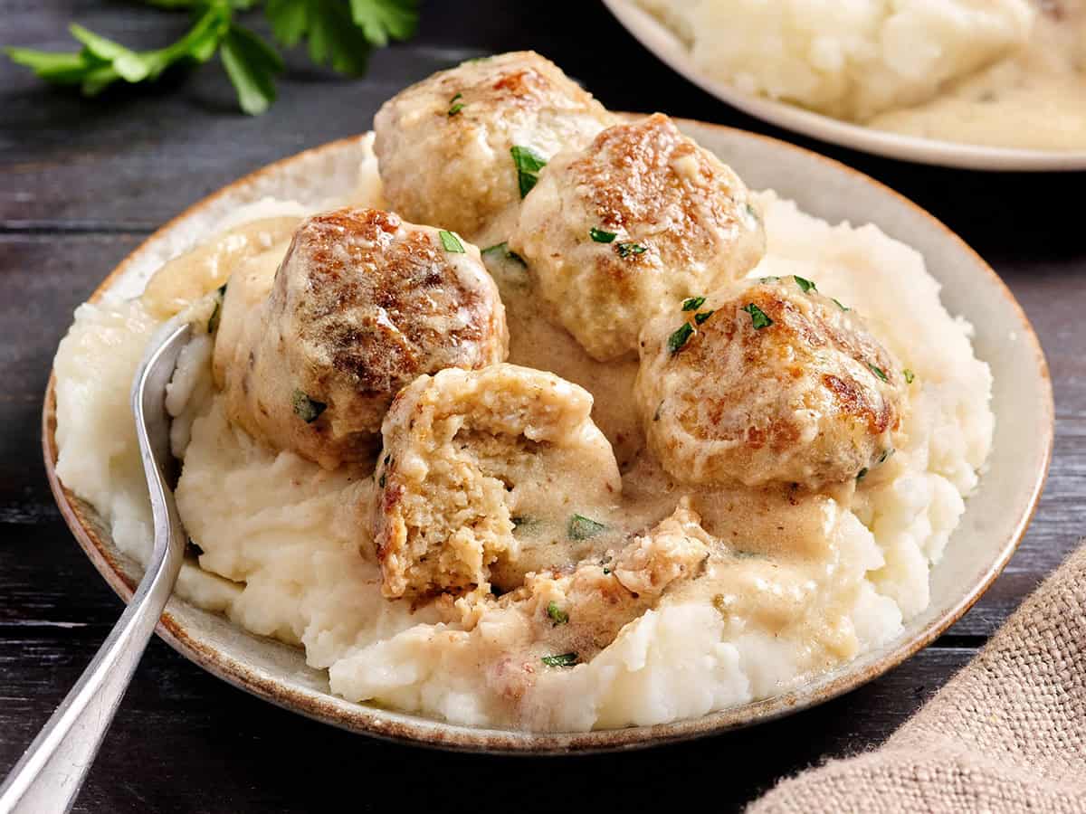 Side view of creamy chicken meatballs on a plate with mashed potatoes.