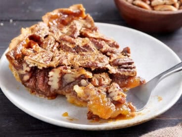 Side view of a slice of pecan pie with a fork taking some.