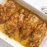 Overhead view of four baked chicken breasts in a baking dish, garnished with fresh parsley.