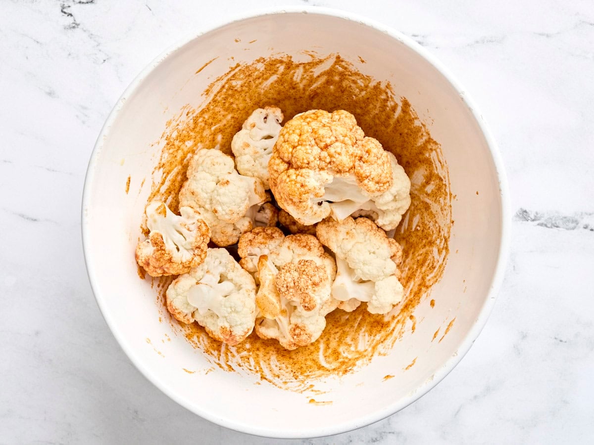 Cauliflower florets coated in a seasoning mix in a bowl.