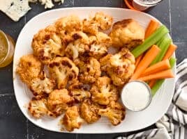 Overhead view of buffalo cauliflower wings on a plate with celery sticks, carrot sticks, and dip.