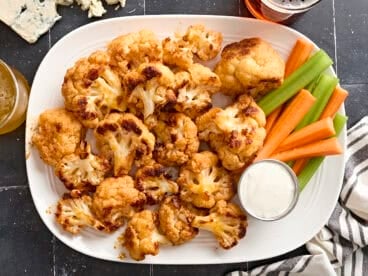 Overhead view of buffalo cauliflower wings on a plate with celery sticks, carrot sticks, and dip.