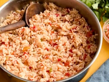 Side view of spanish rice in a skillet with a wooden spoon.