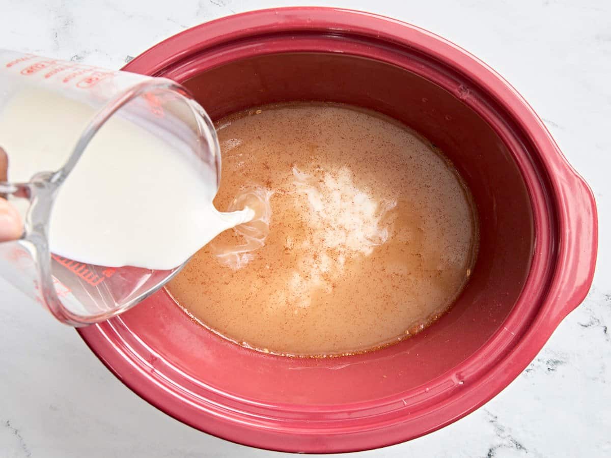 Oats and water in a slow cooker, with milk being poured in.